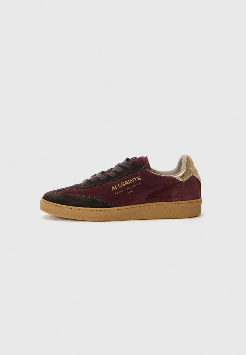 Zapatillas de ante en burdeos oscuro y marrón con detalles en dorado. Presentan una parte superior texturizada, logo en relieve y una suela de goma.