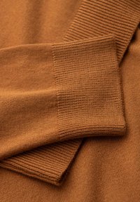 Brauner Strickpulloverstoff mit gerippten Bündchen, der eine glatte Textur und einen subtilen Glanz aufweist. Überlappende Abschnitte zeigen unterschiedliche Muster.