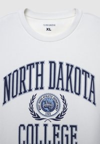 Felpa bianca con colletto rotondo, caratterizzata da testo blu navy "NORTH DAKOTA COLLEGE" e un emblema circolare con dettagli di alloro. Taglia XL.