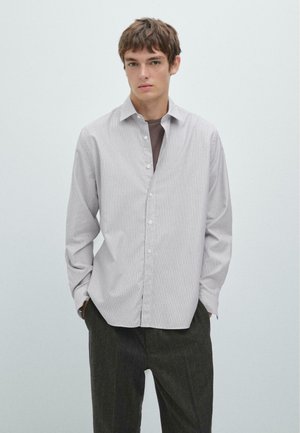 Camicia a righe in grigio chiaro e bianco, con una vestibilità morbida, colletto stretto e maniche lunghe. Indossata con pantaloni scuri e strutturati.