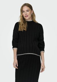 Un pull en tricot noir avec une texture côtelée, doté d'un col montant et de manches trois-quarts, rehaussé de finitions blanches aux poignets et à l'ourlet.