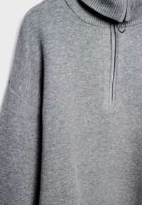 Grauer Pullover mit hohem Kragen, ausgestattet mit einem halben Reißverschluss und strukturiertem Strick. Weiches Material mit überschnittenen Schultern und lockerer Passform.