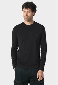 Svart långärmad t-shirt i bomull med rundad halsringning och en liten fyrkantig logotyp på vänster bröst. Slät struktur.