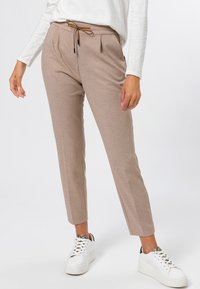 Light brown tapered pants with a drawstring waist, featuring two front pockets and a smooth, soft fabric. Paired with white platform sneakers.