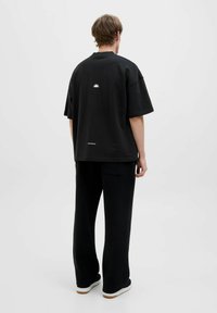 Schwarzes, oversized T-Shirt mit kurzen Ärmeln, das einen Grafikdruck auf dem Rücken trägt und mit schwarzen, weiten Hosen und weißen Sneakers kombiniert ist.