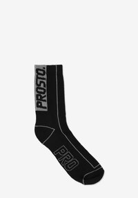 Czarna skarpeta z szarym prążkowanym ściągaczem, na którym widnieją pogrubione napisy "PRO" i "PROSTO". Wykonana z miękkiej tkaniny z wzmocnionym palcem.