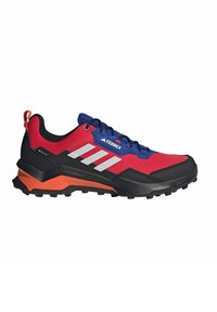Rote und blaue Sportschuhe mit schwarzen Akzenten, strukturiertem Obermaterial, Gummisohle und reflektierenden Details. Verfügt über eine auffällige orangefarbene Fersenschlaufe.