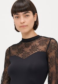 Body negru cu o peliculă din dantelă. Bustul are un decolteu în formă de inimă și mâneci lungi din material transparent cu modele din dantelă florală.