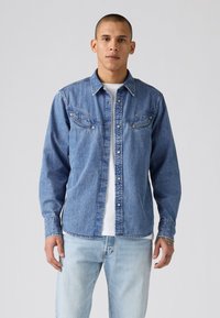 Lichtblauwe denim shirt met een knoopsluiting aan de voorkant, een puntige kraag en twee borstzakken. Heeft metalen drukknopen en een relaxte pasvorm.