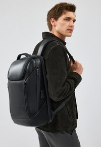 Zaino in pelle nera con un design strutturato, dotato di numerosi scomparti con zip e di una maniglia superiore. Spallacci regolabili.