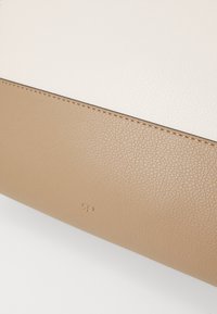 Borsetta rettangolare beige e crema in pelle testurizzata, con dettagli di cucitura e un piccolo logo impresso sul fondo.