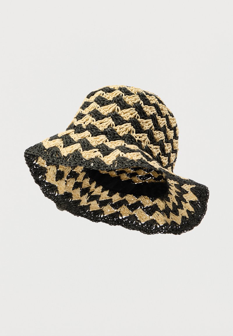 Μαύρο και μπεζ καπέλο κουβάς από πλεγμένο άχυρο με σχέδιο ζιγκ-ζαγκ, διαθέτει φαρδύ γείσο και ανοιχτό πλέγμα για αερισμό.
