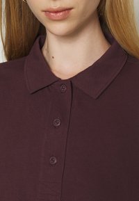 Tmavě bordó polokošile s límečkem, dvěma knoflíky a texturovanou bavlněnou tkaninou s viditelným šitím.