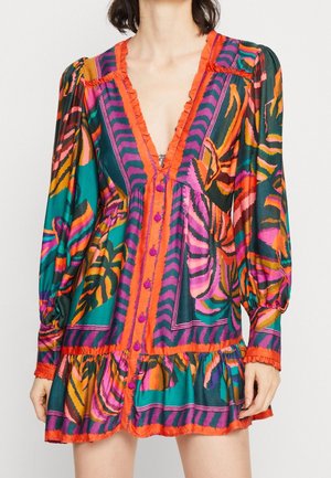 Woman wearing a colorful long-sleeve dress with deep V-neck, featuring orange, pink, green, and purple abstract patterns and ruffle details.
