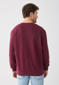 Pull bourgogne à col rond, à manches longues et avec des poignets côtelés, fabriqué en coton doux, présentant une coupe décontractée et des coutures minimales.