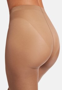 Calze trasparenti semitrasparenti in tonalità nude, caratterizzate da una texture liscia, vita alta e design senza cuciture, che evidenziano una vestibilità aderente.