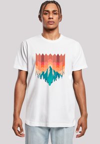 White cotton t-shirt featuring a colorful graphic of mountains and trees with geometric patterns in shades of pink, orange, and teal.
