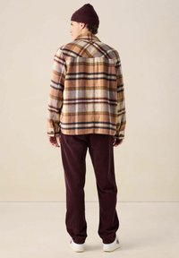 Geruit flanellen overhemd in aardetinten met bruine, crème en blauwe patronen, gecombineerd met bordeauxrode corduroy broek en witte sneakers.