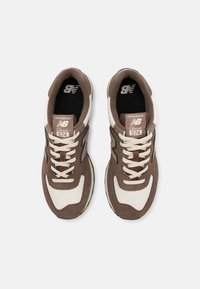 Smeđe i krem New Balance 574 tenisice s gornjim dijelovima od mrežice i antilopa, okruglim vezicama i crnim gumenim potplatom. Klasični naglasci s logom.