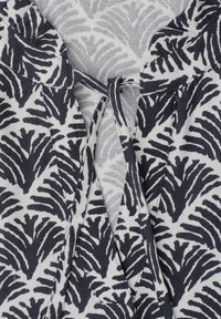 Close-up of black and white fabric with fern-like pattern and a tied loop detail on textured cloth background.
