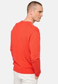 Pull en tricot rouge à col rond, texture légère et manches longues, associé à un pantalon blanc, vu de dos.