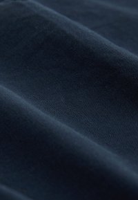 Temno modro tkanino z teksturo, ki prikazuje mehko, gladko površino z vidnimi vzorci tkanja in nežnimi odsevi svetlobe čez gube.