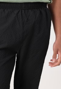 Schwarze, strukturierte Hose mit elastischem Bund. Sie hat eine lockere Passform und seitliche Taschen. Das Material wirkt leicht und strapazierfähig.