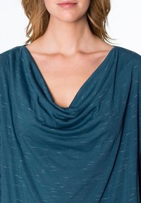 Blouse drapée bleu sarcelle avec un col bénitier, réalisée dans un tissu doux et texturé présentant de subtils éclats blancs partout.