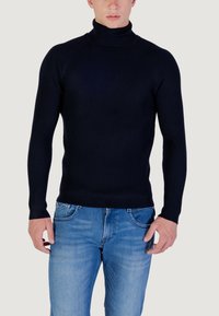 Maglione a collo alto a coste color navy realizzato in un tessuto knit elastico. Presenta maniche lunghe e una vestibilità aderente, abbinato a jeans in denim azzurro.