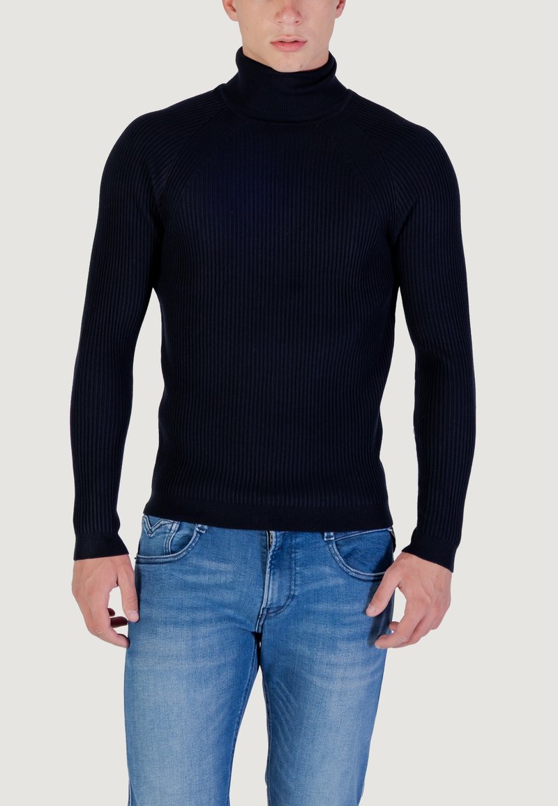 Maglione a collo alto a coste color navy realizzato in un tessuto knit elastico. Presenta maniche lunghe e una vestibilità aderente, abbinato a jeans in denim azzurro.