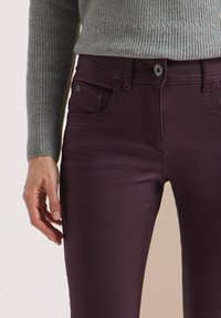 Strakke bordeaux rode jeans met een gladde textuur, knoopsluiting en voorzakken, gecombineerd met een lichtgrijze geribbelde trui.