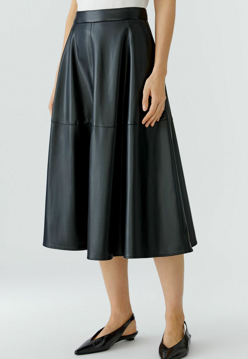 Schwarzer Leder-Midi-Rock mit tailliertem Bund und ausgestelltem Design, ausgestattet mit glatter Textur und Nahtdetails, kombiniert mit schwarzen Slingback-Schuhen.