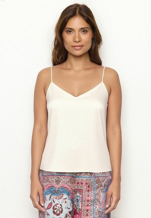 Débardeur beige clair avec un décolleté en V et des bretelles spaghetti fines. Texture lisse, design minimal, associé à un pantalon en tissu à motifs.