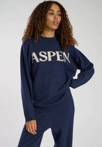 Maglione a maglia blu navy con la scritta "ASPEN" in crema. Vestibilità ampia con polsini e orlo a coste. Texture morbida con un design rilassato.