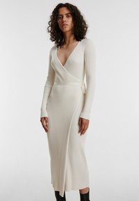 Rippiertes, langärmeliges Wickelkleid in off-white mit tiefem V-Ausschnitt und Taillenknoten, das eine schlanke Silhouette und einen wadenlangen Saum aufweist.