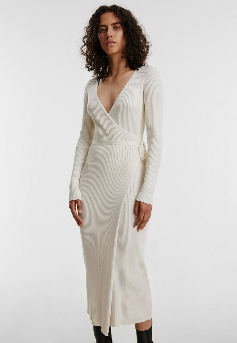 Rippiertes, langärmeliges Wickelkleid in off-white mit tiefem V-Ausschnitt und Taillenknoten, das eine schlanke Silhouette und einen wadenlangen Saum aufweist.