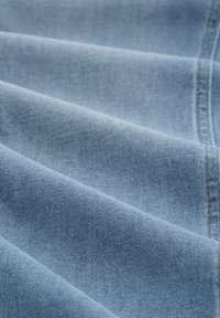 Jasnoniebieska tkanina dżinsowa z widoczną skośną strukturą tkania i przeszyciami, pokazana z bliska z miękkimi fałdami.