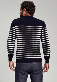 Marineblaues Strickoberteil mit weißen horizontalen Streifen, ausgestattet mit einem runden Ausschnitt und eng anliegenden Bündchen, kombiniert mit dunkelblauen Jeans.