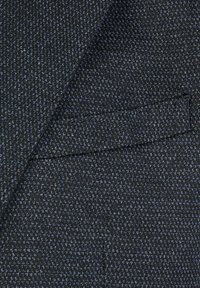 Texturiertes schwarzes Gewebe mit blauen Sprenkeln, das ein glattes, gewebtes Muster aufweist. Enthält ein maßgeschneidertes Taschen-Detail.