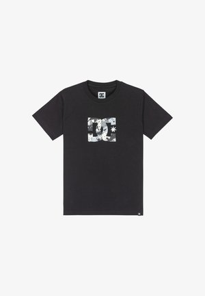 Camiseta de algodón negra con un logo blanco de DC en el centro, que incluye una estrella y un patrón abstracto. Manga corta, diseño de cuello redondo.