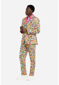 Completo colorato con pois in rosa, giallo, verde, blu e arancione. Presenta una camicia coordinata e scarpe da ginnastica bianche. Vestibilità su misura.