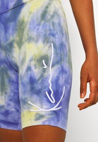 Purple and yellow tie-dye biker shorts made of soft fabric, featuring a white embroidered design on the side and a fitted silhouette.