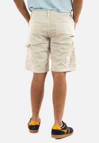 Shorts cargo beiges avec de multiples poches, une coupe décontractée et une longueur au genou. Portés avec des baskets navy et orange avec une semelle en caoutchouc.