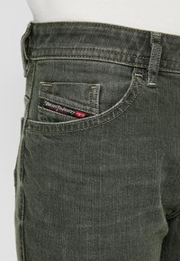 Mörkgröna denimjeans med en figursydd design, med sydda detaljer, en logotypmärke på bakfickan och minimala texturdetaljer.