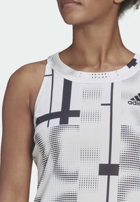 Vit sporttopp i tanktop-stil med svarta geometriska mönster och rund halsringning. Har en mjuk, elastisk textur och minimal detaljering.