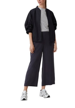 Veste aviateur marine avec des manches bouffantes, associée à un top rayé ajusté et un pantalon large marine. Les accessoires comprennent des baskets blanches.