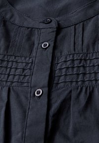 Camicia in tessuto blu navy scuro con bottoni frontali, caratterizzata da dettagli plissettati e ulteriore tessuto arricciato sotto i bottoni.