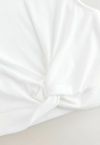 Hvid struktureret stof med en snoet knudedetalje ved kanten, hvilket skaber et indpakket udseende. Glat finish med subtil ribbning.