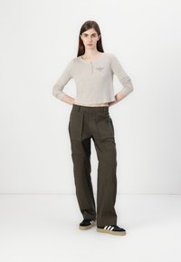 Lys beige, kort langermet skjorte med henley-utførelse og lett tekstur, kombinert med olivengrønne, rette bukser, og svarte joggesko.