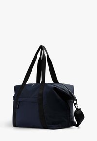 Bolsa de lona azul marino en tela resistente, con correas negras, un bolsillo con cremallera y una correa de hombro ajustable para opciones versátiles de transporte.